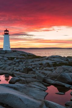 a light house sitting on top of a rocky beach next to the ocean at sunset