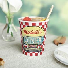 a paper cup filled with ice cream and strawberries on top of a wooden table