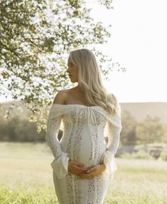 a pregnant woman standing in the grass with her hands on her hips, wearing a white dress