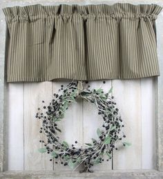 a wreath hanging on the side of a wooden wall next to a window with a striped valance