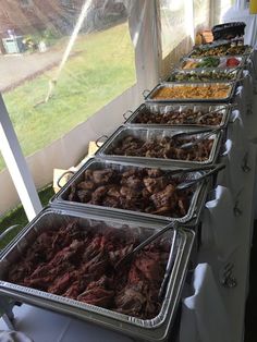 several trays of food are lined up on a table in front of a window