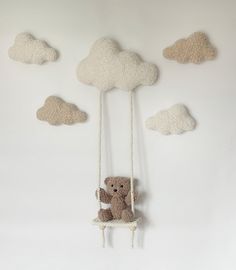 a teddy bear is sitting on a swing in the sky with clouds hanging from it's sides