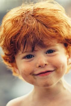 a young boy with red hair smiling at the camera