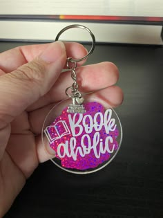 a hand holding a keychain with the words book magic written on it in pink and purple glitter