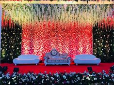 an elaborately decorated stage with two couches and flowers on the floor, in front of a backdrop