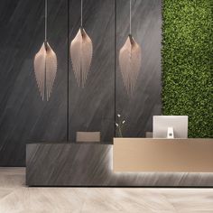 a reception area with three hanging lights and a wooden desk in front of a green wall