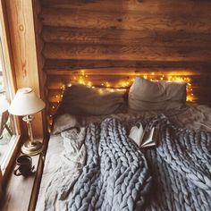 an unmade bed with lights on the headboard and blankets in front of it