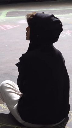 a person sitting on the ground wearing a hoodie and looking at something in the distance