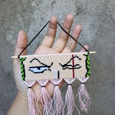 a hand holding a beaded object with two eyes on it's face and tassels