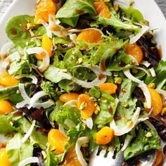 a salad with oranges, onions and lettuce in it on a white plate