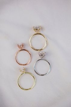 three different colored gold and silver rings on a white surface with one diamond in the middle