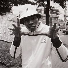 a black and white photo of a man wearing a hat making the peace sign with his hands