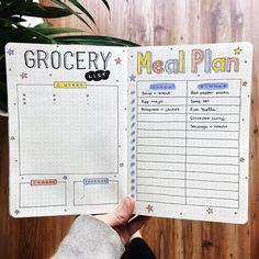 a person holding up a meal planner in front of a wooden table with potted plants