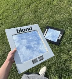 someone is holding up a magazine on the grass with their reflection in the glass window