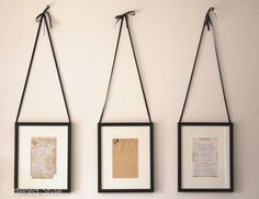 three framed pictures hanging on a wall with twine strings attached to them, and two empty frames