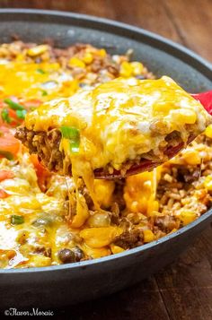 a spoon full of mexican casserole being lifted from a skillet filled with rice