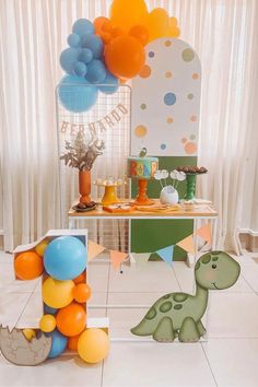 a table topped with balloons next to a dinosaur cake and other decorations on top of it