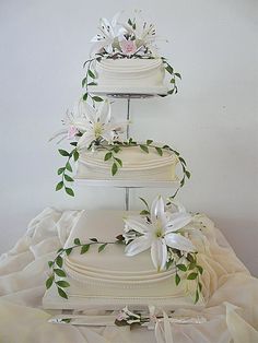 three tiered wedding cake with white flowers and greenery on the top, surrounded by scissors