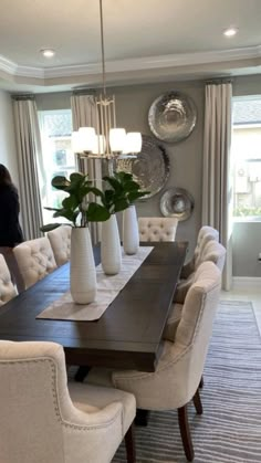 a dining room table surrounded by white chairs and vases with plants in them on top