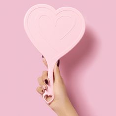 a pink heart shaped object held by a woman's hand on a pink background