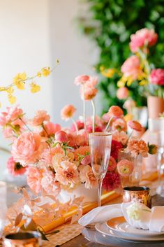 the table is set with pink flowers and champagne glasses, gold place settings and napkins