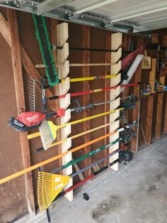 there are many different types of tools hanging on the wall in this garage, including brooms and rakes