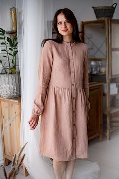 a woman standing in front of a window wearing a pink dress with buttons on it