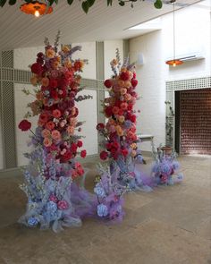 three tall vases filled with colorful flowers sitting on top of a floor next to each other