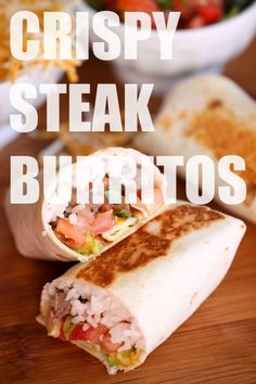 a burrito cut in half sitting on top of a wooden table next to a bowl of salad