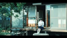 a woman sitting on the ledge of a house looking at her cell phone while wearing a white shirt and blue skirt