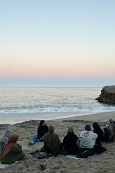 several people sitting on the beach watching the sunset