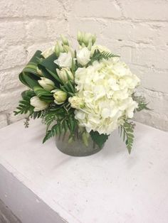 a vase filled with white flowers sitting on top of a table next to a brick wall