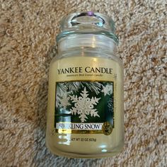 a yankee candle sitting on the floor with snowflakes in it's jar