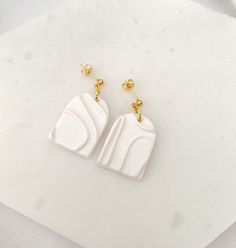 the white and gold earrings are sitting on top of a marble slab, with one earring in the shape of a rectangle