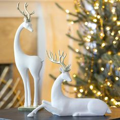 two white deer figurines sitting on top of a table next to a christmas tree