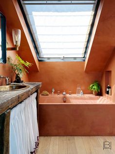 an orange bathroom with a skylight above the bathtub and wooden flooring is shown