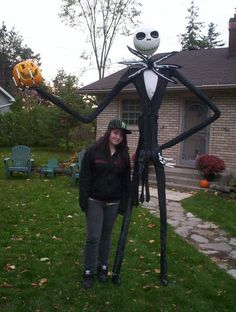 a woman standing in front of a house with a fake skeleton on it's back