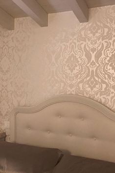 a white bed sitting under a window next to a wall papered with damask