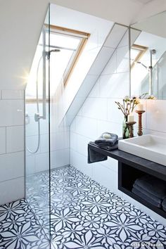 a white bathroom with black and white tile flooring, a skylight and a sink