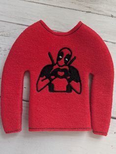 a red sweater with a deadpool design on the front and back, sitting on a white wooden surface