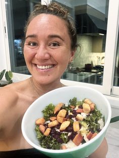 a woman holding a bowl of food in front of her face and smiling at the camera