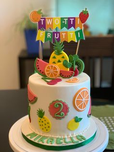 a two tiered cake with fruit decorations on it's top and the words two - tii frutti written in large letters