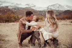 a man and woman kissing their little boy in the middle of a field with mountains in the background