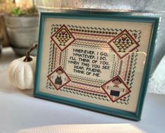 there is a framed cross - stitch pattern on the table next to some pumpkins