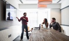 three people sitting at a table with laptops in front of them and one person standing up