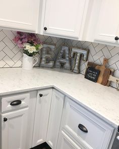 a kitchen with white cabinets and tile backsplash, flowers on the counter top