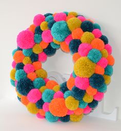 a multicolored pom - pom wreath on a white wall with the letter o