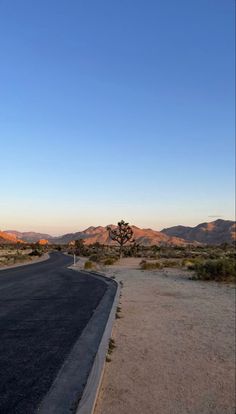 an empty road in the middle of nowhere with mountains in the background