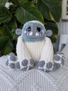 a knitted stuffed animal sitting on top of a white blanket next to a potted plant