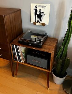 an old record player sits on top of a table next to a cactus